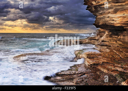 Pazifischen Ozean endlose Wellen untergraben Sandsteinfelsen der australischen Küste in der Nähe von Sydney bei stürmischer Sonnenaufgang Stockfoto