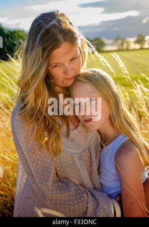 Eine Hintergrundbeleuchtung Porträt einer Frau (Alter 25-30) mit ihrer Tochter (8 Jahre) saß in einem Feld lange Gras auf einen Sommerabend Stockfoto