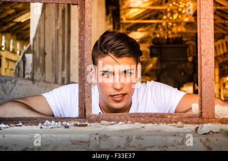 Attraktive Jüngling am rostigen Fenster mit glücklichen Ausdruck auf seinem Gesicht, auf der Suche in der Kamera Stockfoto