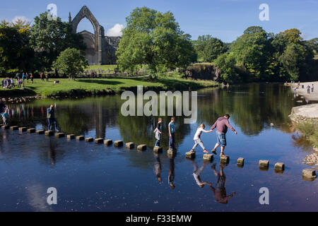 Familien-Risiko fällt in den Fluss Wharfedale während des Gehens über die Trittsteine im Augustiner Bolton Priory, North Yorkshire. Stockfoto