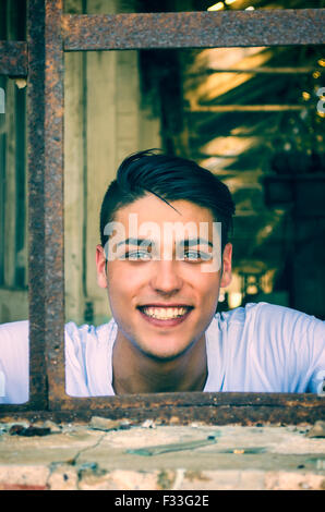 Attraktive Jüngling am rostigen Fenster mit glücklichen Ausdruck auf seinem Gesicht, auf der Suche in der Kamera Stockfoto