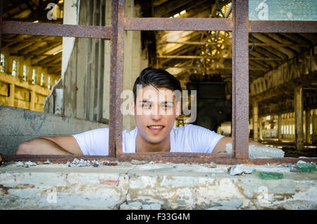 Attraktive Jüngling am rostigen Fenster mit glücklichen Ausdruck auf seinem Gesicht, auf der Suche in der Kamera Stockfoto