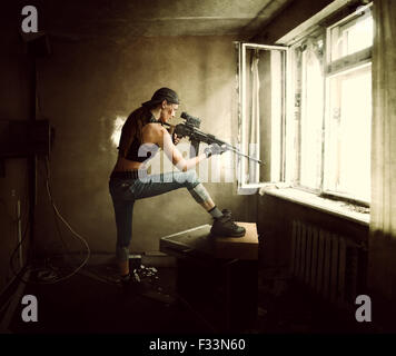 Junge schöne Frau Sniper und Soldat mit dem Ziel einer Gewehrs am Fenster. Sie ist im alten Raum des verlassenen Gebäude Stockfoto