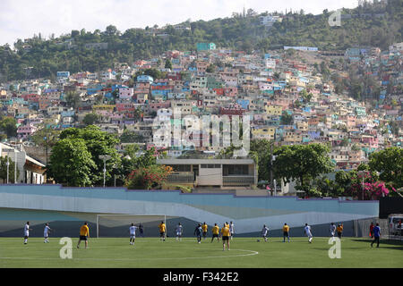 Erwachsene spielen Fußball auf dem Fußballplatz Park Sainte Thérèse mit bunten Häusern entlang der Hügel 15. September 2015 in Port-au-Prince, Haiti. Stockfoto