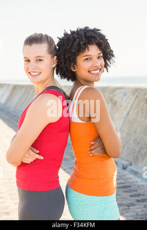 Zwei junge Frauen, die Rücken an Rücken stehen lächelnd Stockfoto