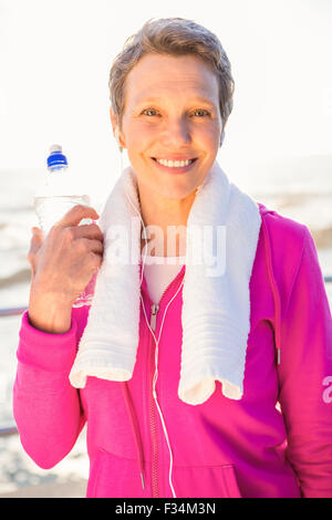 Lächelnde sportliche Frau mit Wasserflasche, Musik hören Stockfoto