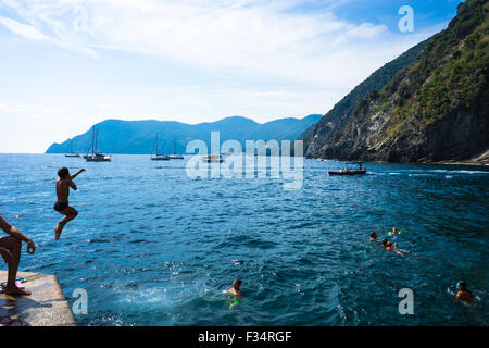 Ein Junge springt aus dem Dock, während Freunde in Vernazza in Italien CInque Terre schwimmen. Stockfoto