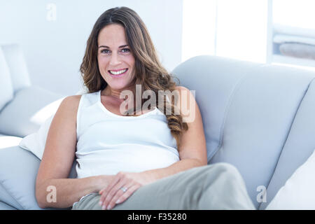 Lächelnde schwangere Frau stützte sich auf sofa Stockfoto