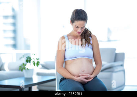 Schwangere Frau betrachten Bauch beim Sitzen auf Stuhl Stockfoto