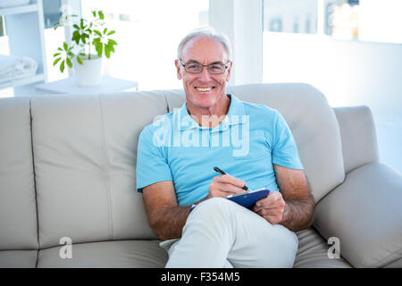 Happy senior woman in Brillen auf Sofa mit Zwischenablage Stockfoto