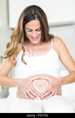 Glückliche Frau mit Herz auf schwangeren Bauch Stockfoto