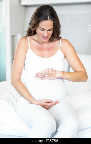 Schwangere Frau auf dem Bett sitzend Stockfoto
