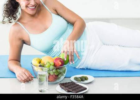 Lächelnde schwangere Frau liegend von Früchten und Schokolade Stockfoto