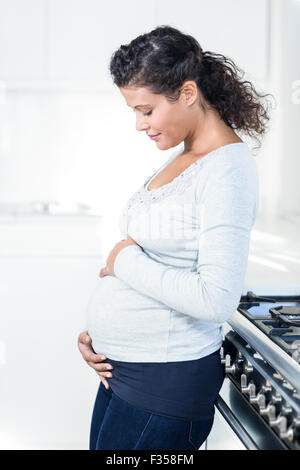 Schwangere Frau berühren ihren Bauch im stehen in der Küche Stockfoto