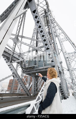 Kaukasischen Frau in ihren 40ern nimmt ein Bild im stehen auf der Antenne Brücke am Lake Superior in Winter, Duluth, Minnesota Stockfoto