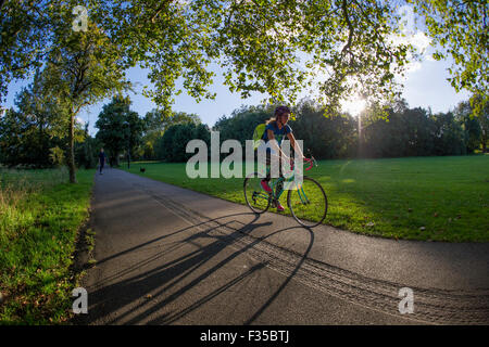 Ein Mädchen-Zyklen in einem Londoner Park mit langen Schatten aus den Sonnenuntergang hinter ihr Stockfoto