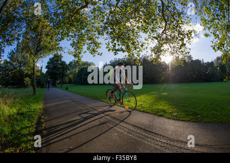 Ein Mädchen-Zyklen in einem Londoner Park mit langen Schatten aus den Sonnenuntergang hinter ihr Stockfoto