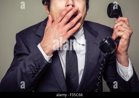 Ein junger Geschäftsmann ist am Telefon und für den Mund unter Schock Stockfoto