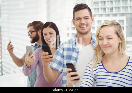 Lächelnde Geschäftsleute mit Smartphones stehend in Reihe Stockfoto