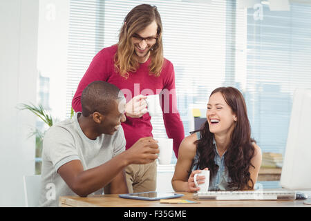 Lächelnde Geschäftsleute halten Kaffeetassen bei Computer-Schreibtisch Stockfoto
