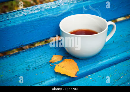 Weiße Tasse schwarzen Tee ist auf alte blaue Holzbank im Herbst Park.  Selektiven Fokus mit flachen DOF, Vintage tonale Fotofilter Stockfoto