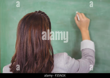 Rückansicht der Lehrer schreibt an die Tafel im Klassenzimmer Stockfoto