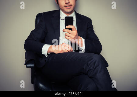 Junger Geschäftsmann, sitzen in einem Bürostuhl ist seine Smartphone verwenden. Stockfoto
