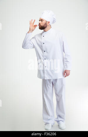 In voller Länge Portrait von einem männlichen Chef-Koch macht leckere Geste durch küssen Fingern isoliert auf weiss Stockfoto