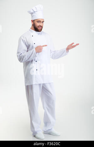 In voller Länge Portrait von happy Chefkoch holding Exemplar auf der Handfläche und Finger drauf isoliert auf einem weißen Hintergrund zu zeigen Stockfoto