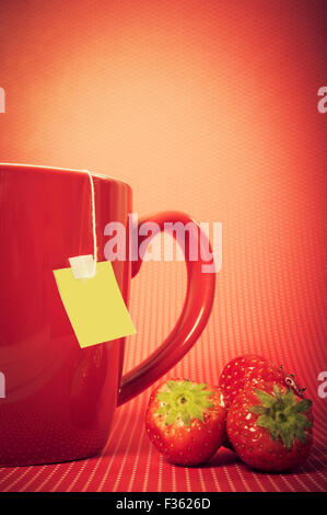 Rote Tasse mit Teebeutel und Erdbeeren, auf rotem Grund Stockfoto