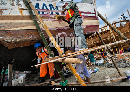 Ecuadorianischen Arbeiter Abdichten eines traditionellen hölzernen Fischereifahrzeug in einer handwerklichen Werft am Strand von Manta, Ecuador. Stockfoto