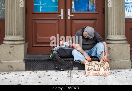 Obdachloser mit einem handgeschriebenen Schild, der halb schläft, auf einer New Yorker Straße Stockfoto