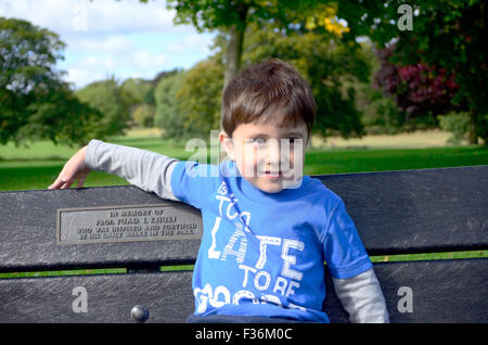 Ein kleiner Junge sitzt auf einer Bank im Park. Stockfoto