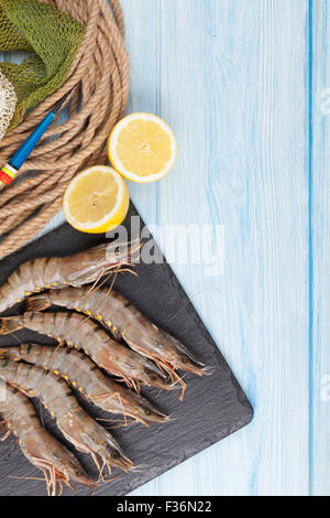 Frische rohe Riesengarnelen und Ausrüstung für die Fischerei auf Holztisch. Draufsicht mit Textfreiraum Stockfoto