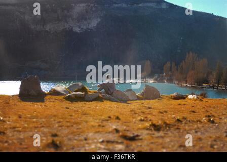 boy sitting in the stones looking the lake big mountain behind Stockfoto
