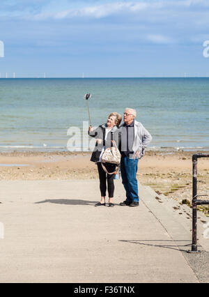 Mitte im Alter von Mann und Frau unter Selfies (Selbstporträt) mit einem Selfie-Stick auf Llandudno Strand Wales, UK. Stockfoto