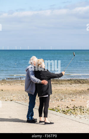 Mitte im Alter von Mann und Frau unter Selfies (Selbstporträt) mit einem Selfie-Stick auf Llandudno Strand Wales, UK. Stockfoto