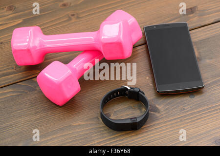 tragbares Gerät, Wirst sehen geben Sports Tracker mit Smartphone und rosa farbigen Hantel auf einem Holzbrett Stockfoto