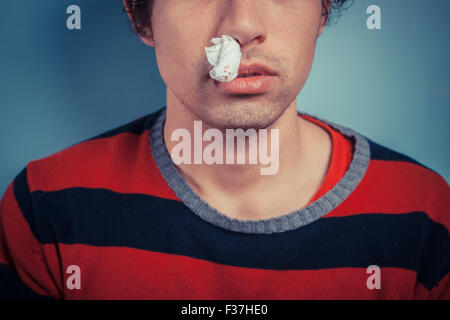 Junger Mann mit Gewebe seine Nasenflügel hat Nasenbluten sowie Fieberbläschen auf seine Lippe Stockfoto