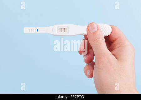 Männliche Hand mit positiven Schwangerschaftstest auf hellblauem Hintergrund isoliert. Glücklicher Vater. Stockfoto