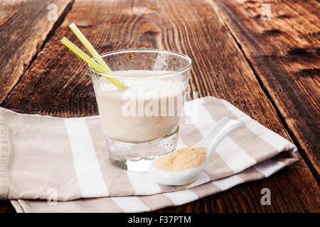 Maca Pulver auf Löffel und Maca Pulver in Milchshake auf Tuch auf braunen Holztisch. Gesundes Wohnen, alternative Medizin, rustikal Stockfoto