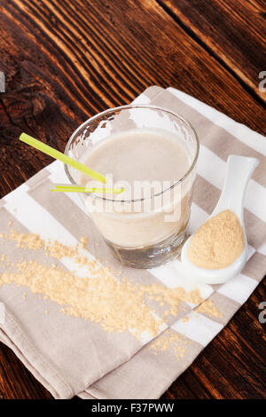 Maca Pulver auf Löffel und Maca Pulver in Milchshake auf Tuch auf braunen Holztisch. Gesundes Wohnen, alternative Medizin Stockfoto