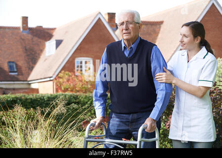 Pflegeperson Senior Menschen helfen, zu wandeln im Garten unter Verwendung des Rahmens zu Fuß Stockfoto