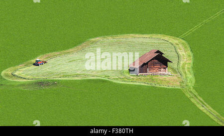 Luftaufnahme des grünen Agrarbereich mit Mähwerk im Kreis um ein Holzhaus. Die Wiese ist gefüllt, die Stockfoto