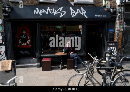 Junger Mann am Telefon sitzen vor einer trendigen Bar in Brick Lane, London E1 Stockfoto