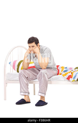 Vertikale Schuss besorgt junger Mann im Schlafanzug, die auf einem Bett sitzend und Betrachtung auf weißen Hintergrund isoliert Stockfoto