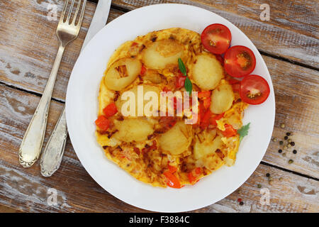 Omelett mit Kartoffeln, Zwiebeln, Paprika und Mais auf weißen Teller auf rustikalen Holzoberfläche Stockfoto