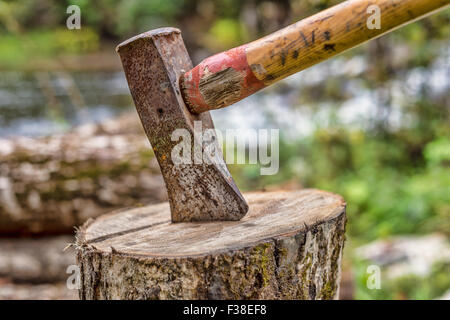 Axt auf Hackstock mit einem Holzstapel im Hintergrund Stockfoto