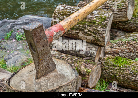 Axt auf Hackstock mit einem Holzstapel im Hintergrund Stockfoto