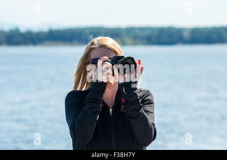 Schöne blonde Frau, die das Fotografieren draußen am Wasser Stockfoto
